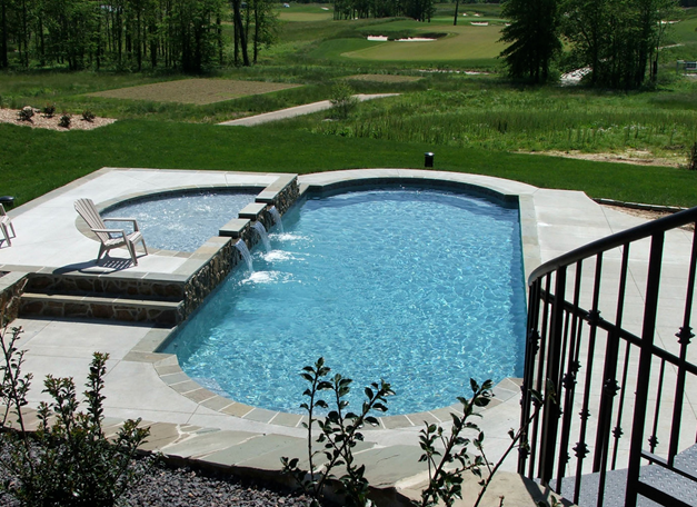 This classically shaped fiberglass pool features a raised bond beam with sheer descents, a concrete deck and stone coping.