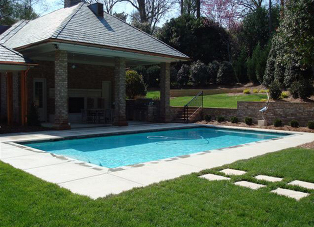 This swimming pool features a white plaster finish with stone coping, concrete decking, seating, and an outdoor kitchen.