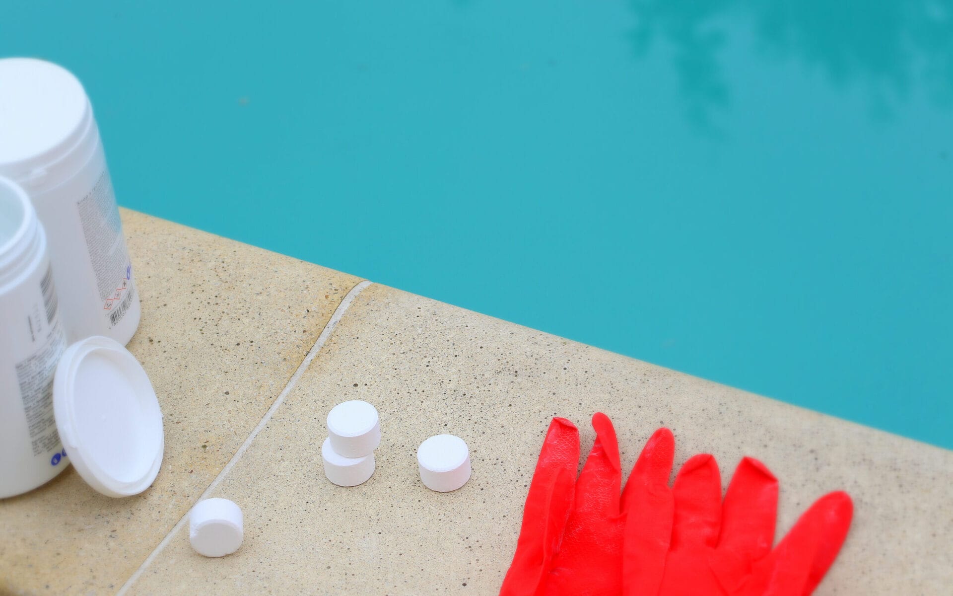 White mini-tablet of chlorine in the hand of the staff for disinfection of swimming pools. The beginning of the swimming season is hot summer. Rubber protective red glove. Water purification.