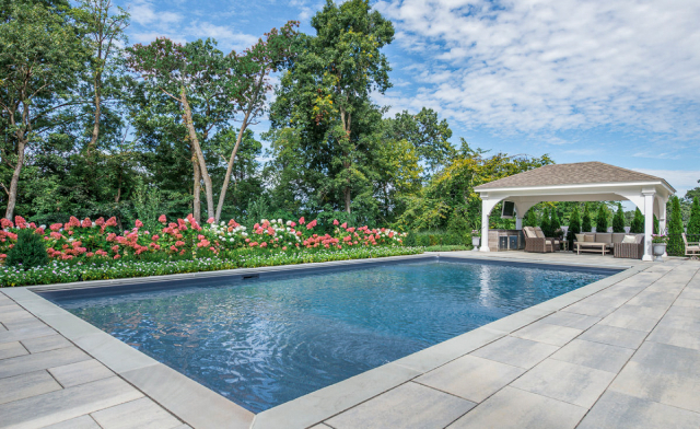 Backyard swimming pool with stone patio, flowers, and gazebo.