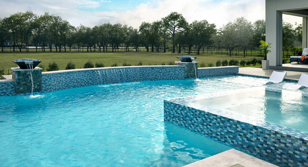 Backyard swimming pool with waterfall feature, lounge chairs, and green lawn.