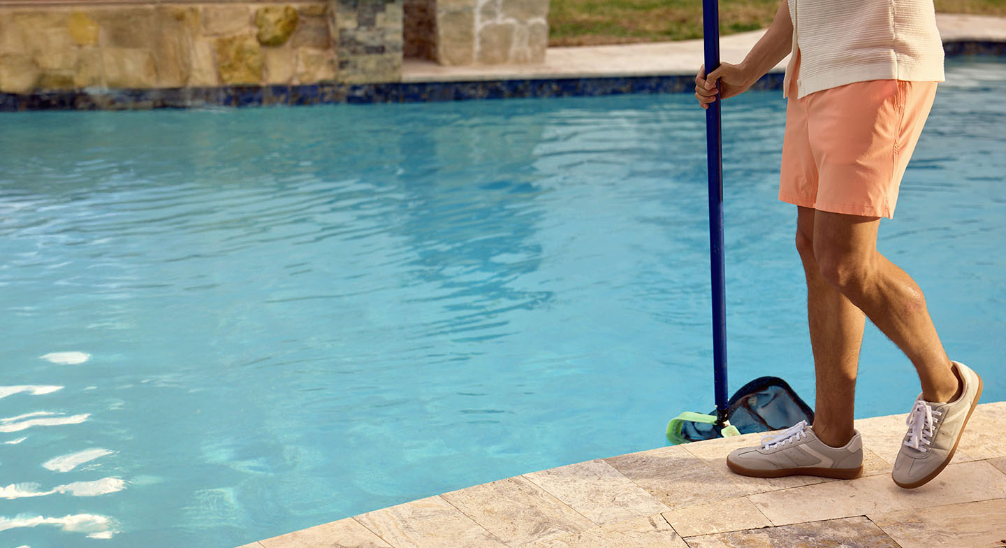 Man cleaning swimming pool with skimmer